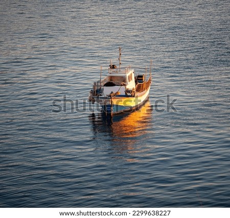 Moored fishingboat in the middle of ripple blue Aegean sea. Colorful sparkle water from sunbeam, reflection of boat, Cyclades island, Greece.