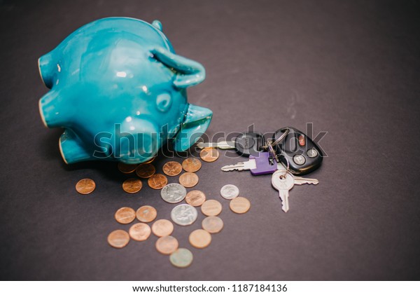 Mooresville, IN USA 09 23 2018: Piggy\
Bank with money and a set of car keys. Black background. Blue piggy\
bank with coins and keys. Car insurance\
money