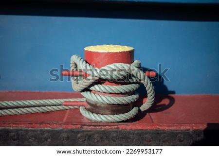 A mooring bollard entwined with a mooring rope. Moored ships at the port quay. Season winter.