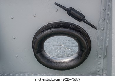 Mooring fairlead with round hole and black cast-iron ring with smooth rounding on ship is installed in gray riveted bulwark. Above is casted horn nearby. Sea water is visible in opening of fairlead. - Shutterstock ID 2026745879