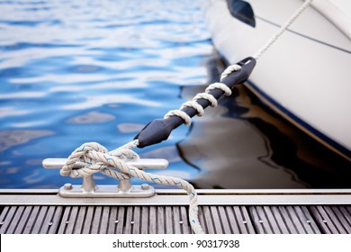 Mooring at a pier/ A white yacht moored with a line tied around a metal fixing on the quayside.