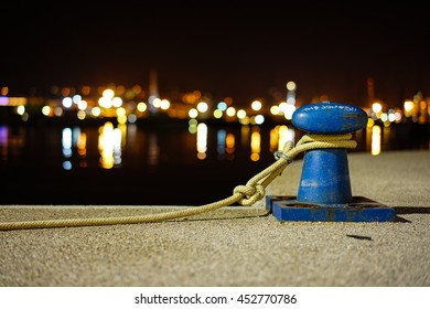 Mooring rope with a knotted end tied around a cleat on a cement pier/ Nautical mooring rope,Abstract blurred night view of city wharf lights, inverted image and coastline skyline as background.
