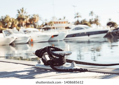 Mooring yacht rope with a knotted end tied around a cleat on a wooden pier against marina view