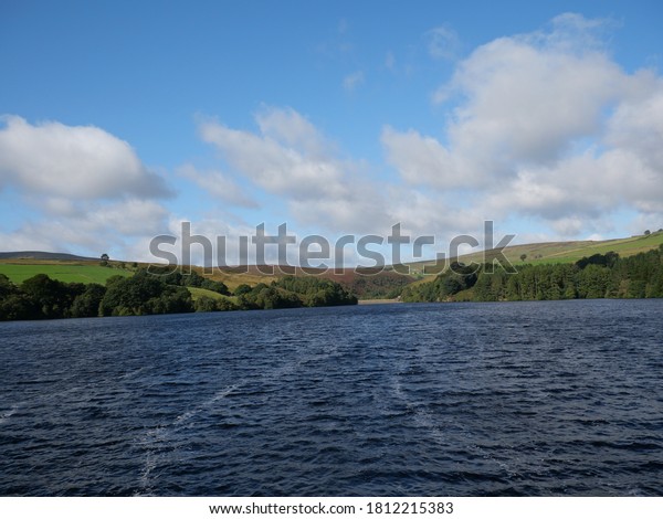Moorland reservoir with blue\
water and white wind lanes distant trees and moors blue sky and\
white clouds Huddersfield Yorkshire England 09/09/2020 by Roy\
Hinchliffe