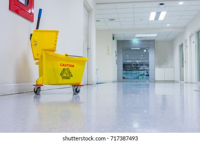 Mop bucket and wringer with caution sign on black floor in walkway office building.