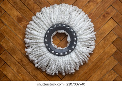 Mop head with wringer, made of white microfiber, for cleaning the floor, against the background of old parquet