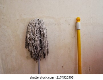 Un palo de cortar parado gris contra una pared. Al lado había un palo amarillo de una escoba.
