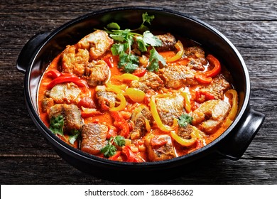 Moqueca baiana - brazilian fish stew of white fish with sweet pepper, lime juice, chopped tomatoes, coconut milk, served on a black dish with cilantro on a dark wooden background, top view