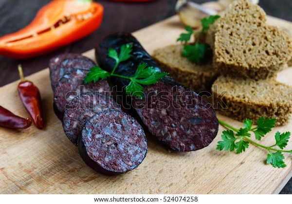 Morcillo (Spanish black pudding, blood sausage),\
cutting slices, black rye bread in a heart shape, pepper, garlic on\
a wooden board. Close\
up