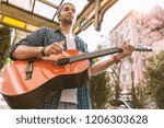 More practice. Low angle of handsome male guitarist walking on street and playing on guitar