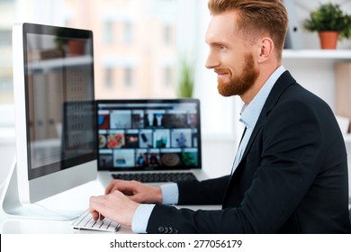 It is more than just a job. Side view of bearded businessman working on computer and smiling while sitting at his working place - Powered by Shutterstock