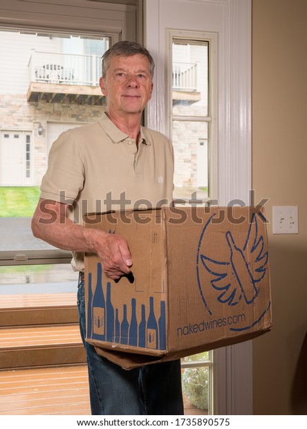 Stock photo of senior man carrying a case of wine into his home