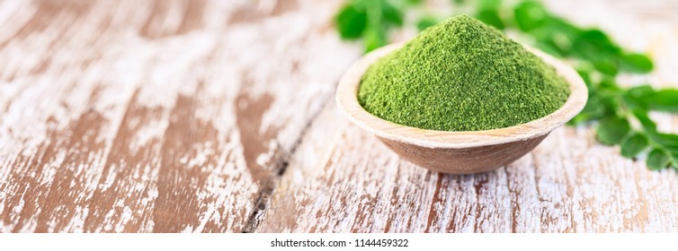 Moringa powder (Moringa Oleifera) in coconut bowl with original fresh Moringa leaves on wooden background. Healthy product, superfood, vitamin. Long banner space for text.