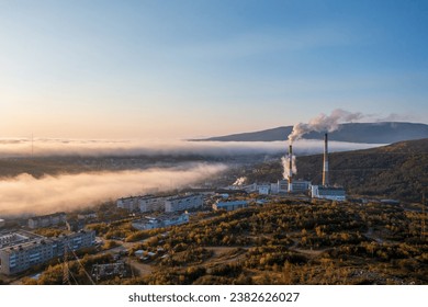 Morning aerial photograph of a combined heat and power plant on the outskirts of the city. Top view of smoking chimneys and residential buildings. Low clouds. Magadan, Magadan region, Siberia, Russia. - Shutterstock ID 2382626027