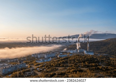 Morning aerial photograph of a combined heat and power plant on the outskirts of the city. Top view of smoking chimneys and residential buildings. Low clouds. Magadan, Magadan region, Siberia, Russia.