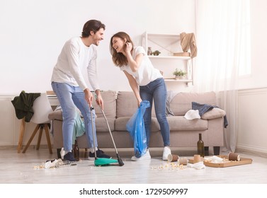 Morning After Party. Laughing Young Couple Cleaning Mess In Their Flat After Celebration At Home, Copy Space