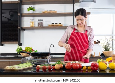 Morning atmosphere in a modern kitchen. beautiful Asian woman stands in a kitchen cooking wearing a red apron. The healthy menu she will cook is salmon, steak and salad. Modern woman kitchen concept