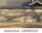 Morning and autumnal view of grass and sunlight and shadow on stonewall of tile-roofed house at Jongmyo Shrine, Seoul, South Korea
