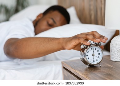 Morning Awakening. Sleepy Black Man Turning Off Alarm Clock Waking Up Early Lying In Bed In Bedroom At Home. Time To Wake-Up And Get Up Concept. Shallow Depth