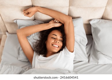 Morning Awakening. Well rested african american woman leisurely wakes up stretching her arms in bed at home, enjoying morning awakening in domestic bedroom interior. Good sleep and recreation - Powered by Shutterstock