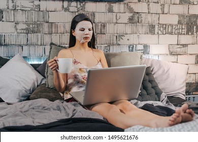 Morning Beauty Routine For A Business Woman Laying Down On The Bed With A Faces Mask On Working On Her Laptop While Drinking Some Coffee.