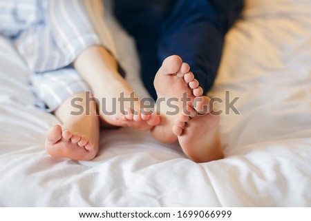 Morning bliss in bed: the heels of men and women, legs in pajamas. The couple wakes up together. No faces.