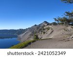 Morning blue sky reflects in Crater Lake, Crater Lake National Park, in Oregon.  Pumice cliffs meat the water.