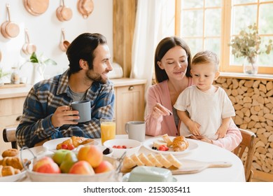Morning breakfast at home. Young caucasian family of three, parents and infant toddler new born baby eating together, feeding son daughter at home kitchen. Parenthood concept - Shutterstock ID 2153035411