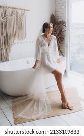 Morning of the bride in a rustic style, in a white bathrobe and a white bouquet on the bed and in the bathroom by the window in a photo studio, in a hotel