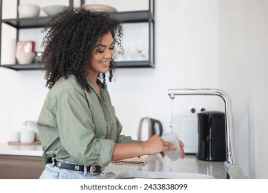 Morning Chores. Happy Brazilian woman stands by the sink washing cup, doing dishes at home kitchen. Lady tackles her daily routine in modern apartment interior. Daily housework - Powered by Shutterstock