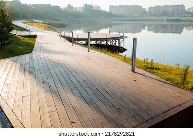 Morning in the city park, a pedestrian road of boards runs along the lake, a round pier for boats, a wooden pier on the water, the design of the park in nature. High quality photo