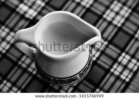 A painted ceramic milk jug next to an empty white cup