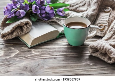  Morning Coffee. A Cup Of Coffee On A Wooden Table, An Open Book And A Warm Sweater Against The Background Of A Bouquet Of Spring Flowers. Still Life Concept. Cozy Morning. 