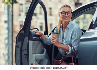 Morning With Coffee. Fashionable Smiling Middle Aged Business Woman Holding Paper Cup Of Coffee And Getting Out Of Her Car, She Is Arriving At Work