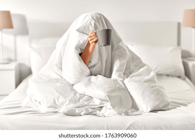 morning, comfort and people concept - young woman with cup of coffee sitting in bed under blanket at home bedroom - Shutterstock ID 1763909060