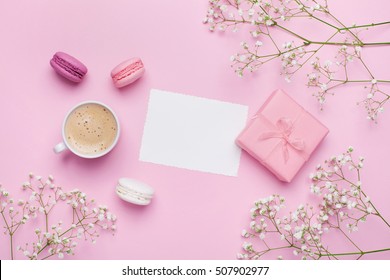 Morning cup of coffee, cake macaron, gift or present box and flower on pink table from above. Beautiful breakfast. Flat lay style.