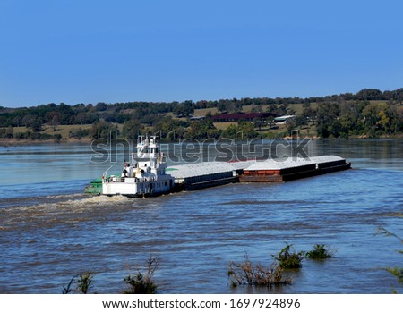 Morning departure has tugboat, also called a pusher, moving cargo up the Mississippi River in Arkansas.  Tugboat is white and has multiple shipments attached.