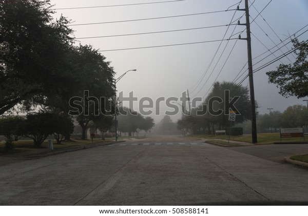 Morning foggy city road with traffic sign and\
car silhouette in Houston, Texas, US. Driving with caution in bad\
weather. Foggy hazy transportation hazard. Severe weather theme\
concept background.