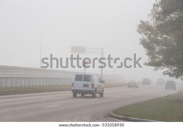 Morning foggy city road with traffic sign and\
car silhouette in Humble, Texas, US. Driving with caution in bad\
weather. Foggy hazy transportation hazard. Severe weather theme\
concept background.