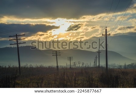 Morning foggy landscape with old telephone poles, some of them are broken. The rising sun illuminated the clouds beautifully.