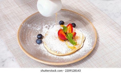 Morning Food, Sweet Breakfast. Woman Hands Pouring Maple Syrup Onto Baked Pancake With Fresh Berries. Honey Tasty Pancake With Strawberry In Cafe. Slow Motion