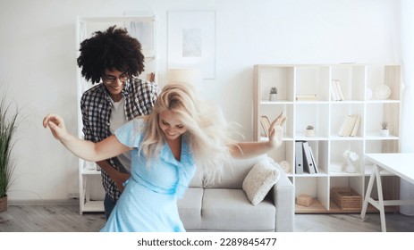 Morning fun. Home joy. Positive lifestyle. Inspired happy energetic diverse couple enjoying dancing spending life moments together in light room interior. - Powered by Shutterstock