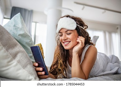 Morning with gadget. Overhead of beautiful young woman lying on the bed using smartphone. Young woman checking her smart phone lying in bed. Happy girl using a mobile phone lying on the bed at home