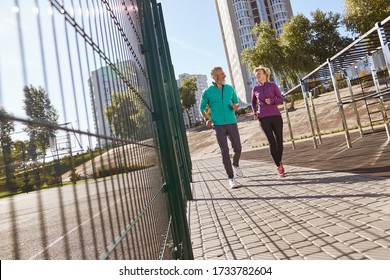 Morning Jog. Active Mature Family Couple In Sportswear Running Together At The Stadium In The Early Morning. Full Length. Beautiful Seniour Couple Doing Sport Outdoors