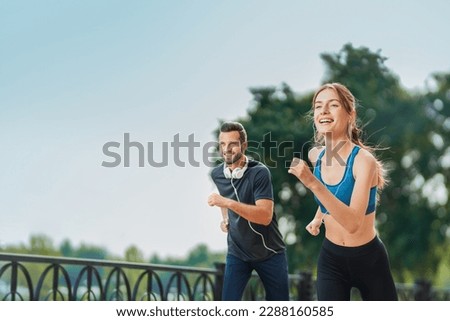 Morning jogging. Image of happy excited smiling young couple, runners running together, woman train with man, or bearded fit coach exercising outdoors. Fitness, sport city marathon workout concept.