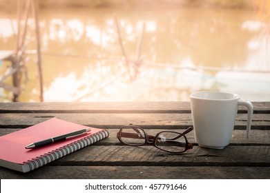 Morning lifestyle scene. Pen, opened notebook, glasses, and coffee cup on outdoor wood table in morning time on weekend. Freelance business working concept - Powered by Shutterstock