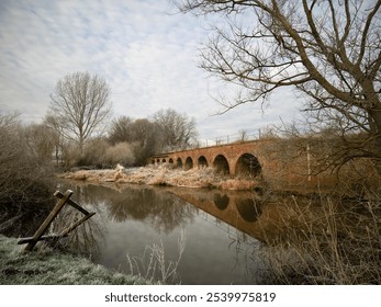 Morning light on river flowing next to disused railway bridge with tunnels beneath - Powered by Shutterstock