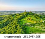 Morning light reveals the impressive ruins of Trosky Castle, perched atop green hills in Bohemian Paradise, surrounded by lush forests and scenic valleys that stretch into the horizon.