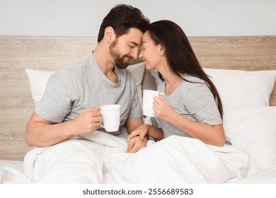 Morning of loving couple with cups of coffee lying in bedroom - Powered by Shutterstock