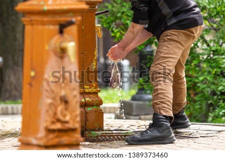 in the morning a man washes his hands and washes himself at a source located in a city park